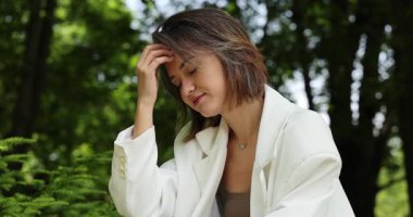 Kamu parkında poz veren beyaz takım elbiseli çekici bir kadın.