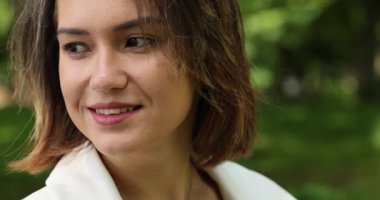 Kamu parkında poz veren beyaz takım elbiseli çekici bir kadın.