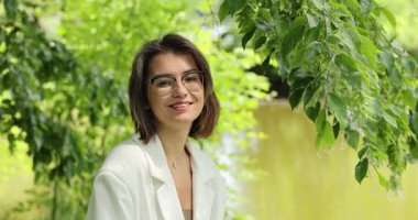 Beyaz takım elbiseli çekici bir kadın gölün arka planında poz veriyor.