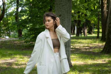 Kamu parkında poz veren beyaz takım elbiseli çekici bir kadın.