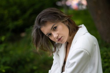 Kamu parkında poz veren beyaz takım elbiseli çekici bir kadın.