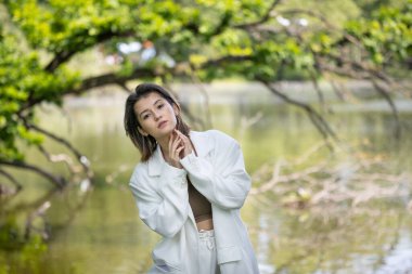 Beyaz takım elbiseli çekici bir kadın gölün arka planında poz veriyor.