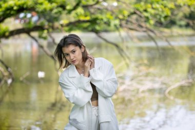 Beyaz takım elbiseli çekici bir kadın gölün arka planında poz veriyor.