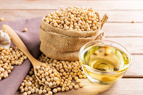 Soybean oil in a glass bowl and soybean seeds in sacks with a wooden spoon placed on a wooden table Natural healthy food - top view