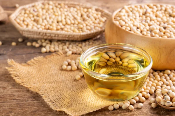 Soybean oil in a glass bowl and soybean seeds in a sack on a wooden table, natural healthy food - top view