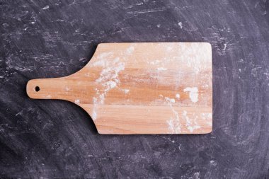 Wooden chopping board and spread of flour on black background table