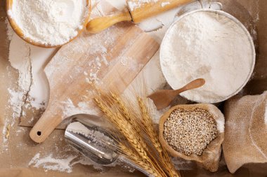 Flour in a bowl and wheat grains with wheat ears on the table, paper background In a rustic kitchen, top view