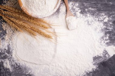 Heaps of wheat flour with ears of wheat on the table, black background - top view