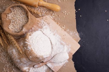 Flour and wheat grains in sacks with wheat ears On a black background table. In a rustic kitchen. Top view.