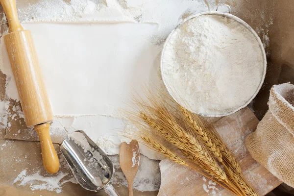 Flour in a bowl and wheat grains with wheat ears on the table, paper background In a rustic kitchen, top view