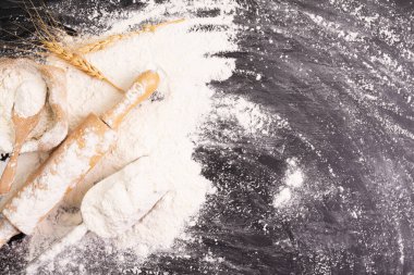 Heaps of wheat flour with ears of wheat on the table, black background - top view