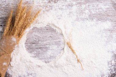 Buğday, arpa, pişirme, ekmek ve kurabiyelerden oluşan un ve kulaklar kırsal bir mutfaktaki ahşap masa zemininde düzenlendi. Üst görünüm.