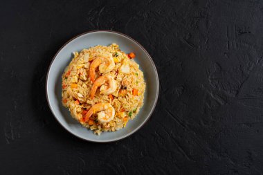 Sebzeli pilav ve deniz karidesi, havuç, yumurta ve domates. Tayland Çin yemekleri siyah bir tabakta, arka planda mutfak masasında, üst tarafta..