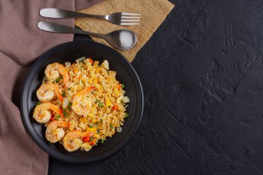Siyah tabakta sebzeli ve karidesli kızarmış pirinç. Masada yatıyordu. Siyah arkaplan - üst görünüm.