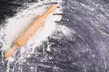 Heaps of wheat flour with ears of wheat on the table, black background - top view