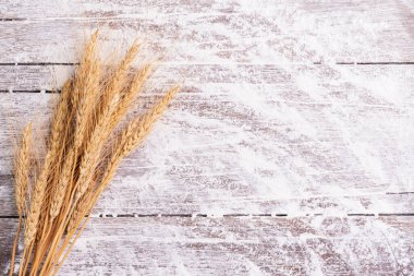 Buğday, arpa, pişirme, ekmek ve kurabiyelerden oluşan un ve kulaklar kırsal bir mutfaktaki ahşap masa zemininde düzenlendi. Üst görünüm.