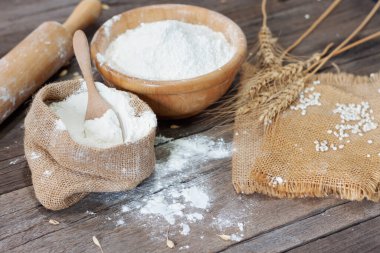 Yumuşak odak, torbalar halinde un, buğday, arpa, yemek pişirme, ekmek ve kurabiyeler kırsal bir mutfakta ahşap bir masanın üstüne dizilmiş..