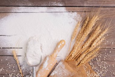 Buğday, arpa, pişirme, ekmek ve kurabiyelerden oluşan un ve kulaklar kırsal bir mutfaktaki ahşap masa zemininde düzenlendi. Üst görünüm.