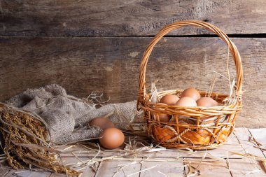 Bir sepet taze yumurta ve kurutulmuş kamışla birlikte organik bir çiftlikteki ahşap bir arka plan masasında duran tavuk yumurtaları.