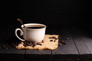 Taze demlenmiş kahve. Kahve fincanı ya da kupa kavrulmuş kahve çekirdekleri ile birlikte siyah ahşap bir masaya dizilmiş. Espresso mocha cappuccino barista koyu arkaplanda.