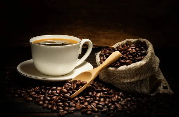 Siyah kahve ya da kapuçino espresso bardağında sıcak çay, kahve çekirdekli kahvaltı, ahşap bir masada koyu bir arka planda izole edilmiş, üst manzara.