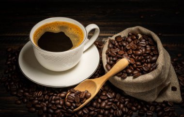 Siyah kahve ya da kapuçino espresso bardağında sıcak çay, kahve çekirdekli kahvaltı, ahşap bir masada koyu bir arka planda izole edilmiş, üst manzara.