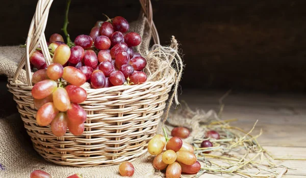 Red grapes, naturally sweet fruit, are placed on a wooden table and arranged in a wooden basket. on the old wooden background