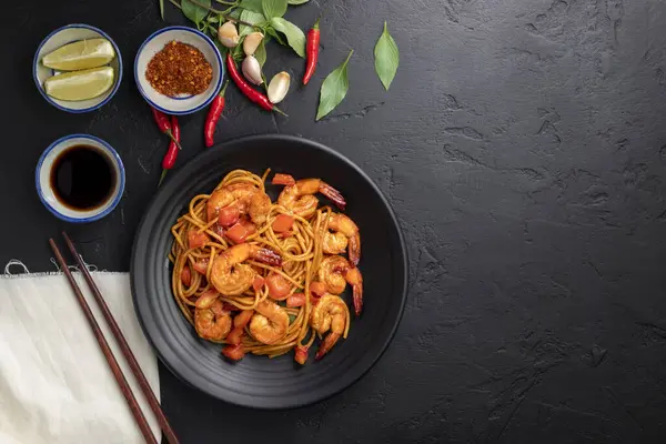 Kızarmış spagetti ya da kızarmış erişte ve siyah arka planda bir tabakta karides. Üst görünüm.