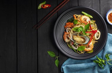 Karides, kalamar, biber ve fesleğenli deniz mahsullü spagetti. Tayland yemeği. Siyah arka plan masasında tabakta sağlıklı bir Asyalı. Üst görünüm.