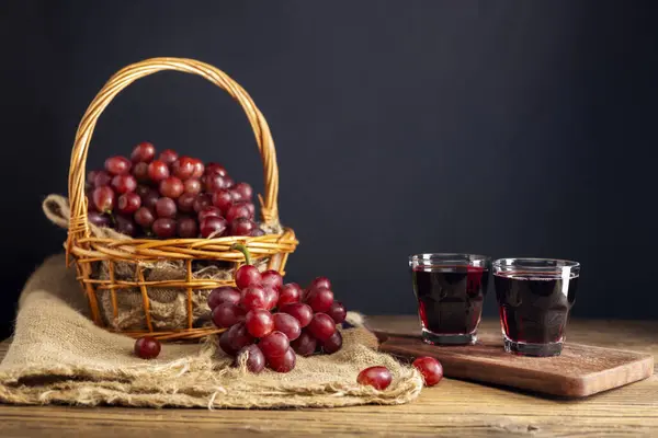 Red grape juice in a glass placed on a wooden table or red wine, a delicious natural healthy juice drink. With a bunch of fresh red grapes from the garden