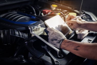 Tamirci, tablet bilgisayar teknolojisi kullanarak motoru kontrol ediyor. Garajda çalışan ingiliz anahtarı tamircisiyle birlikte. Onarım servisi.