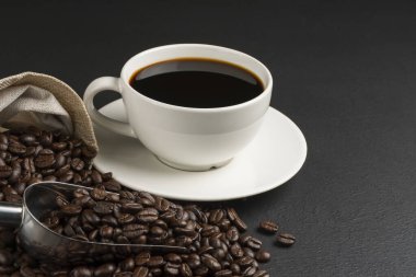 Beyaz kahve fincanında sade kahve ve siyah masa manzarasında kavrulmuş kahve çekirdekleri