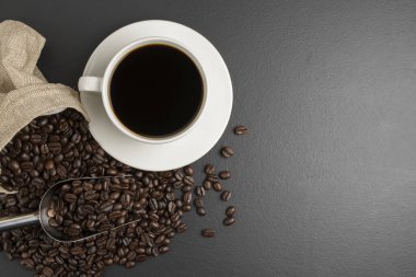 Sütlü kahve fincanında sade kahve ve kavrulmuş kahve çekirdekleri siyah masanın üzerinde, üstteki görüntüde mesajlarınız için yer var.