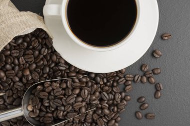 Beyaz kahve fincanında sade kahve ve siyah masa manzarasında kavrulmuş kahve çekirdekleri