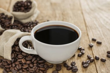 Beyaz kahve fincanında sade kahve ve ahşap bir masanın üstüne kızarmış kahve çekirdekleri.