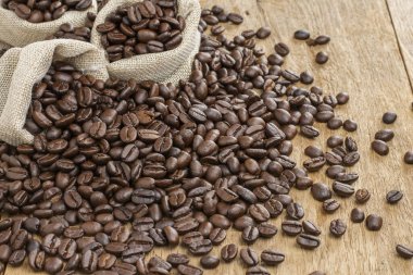 Kavrulmuş kahve çekirdekleri ve kahve poşetleri ahşap bir masaya yerleştirilmiş..