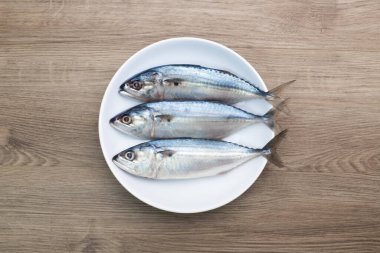 Taze uskumru, beyaz bir tabakta doğal deniz ürünleri ve ahşap zemin üzerinde buzla süslenmiş fesleğen. Üst görünüm.