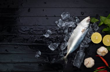 Taze uskumru, siyah ahşap zemin üzerine dizilmiş buzla birlikte siyah bir tabakta duran doğal deniz ürünleri. Üst görünüm.