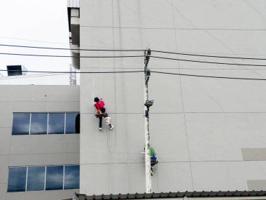 Duvarı tamir eden ve inşaat işçisinin duvarını boyayan boyacı. Paten fırçasıyla yüksek binalarda güvenlik ekipmanı olmadan çalışıyor. Yükseklerde tehlikeli iş kavramı.