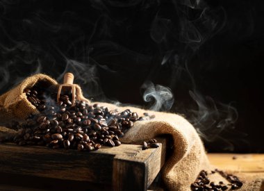 Masanın üstünde kavrulmuş kahve çekirdekleri, siyah arka plan ve koyu renkler.