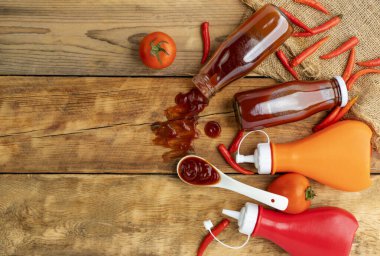 Ketçap, acı biber sosu, plastik sos şişeleri ve cam şişeler mutfaktaki ahşap masa, üst manzara.