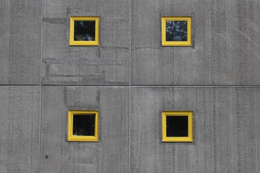 Beton bir duvarda dört sarı çerçeveli küçük pencereler.