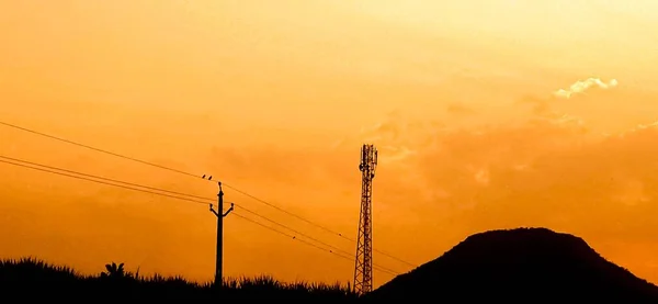 Gün batımında gökyüzü arka planında yüksek voltajlı elektrik direğinin silueti.