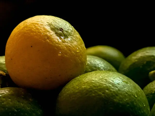 Yellow lemon in group of green lemons with black background