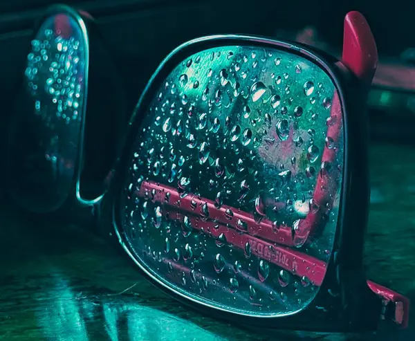 Aqua kırmızısı gözlük camlarına yağmur damlaları düşer. Bilgisayarın mavi gözlüklü camları yere vurur.