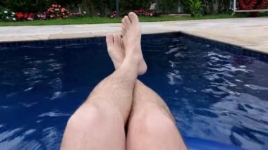 Adam şamandırada oturuyor, bacakları açık, havuzda dinleniyor..