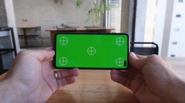 Erkek el ele tutuşuyor ve yatay olarak smatfon izliyor, yeşil ekran ve işaretlerle.