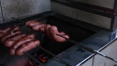 Bifteğin üzerindeki domuz sosisleri Brezilya barbeküsünde diğer tarafı pişirmek için çevriliyor..