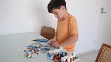 Turuncu pijamalı 10 yaşındaki Brezilyalı çocuk yapı taşlarıyla oynuyor..