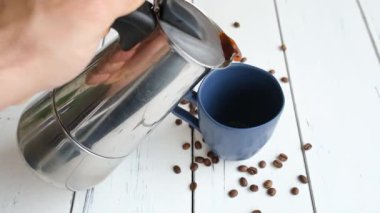 Kahvesini koyu mavi bardağa dolduran adam beyaz ahşap bir masada..